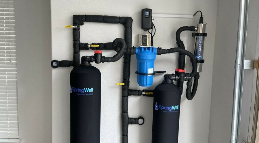 Water filtration system with SpringWell branding, featuring black tanks, blue filter, and connected piping, illustrating plumbing solutions for improved water quality.