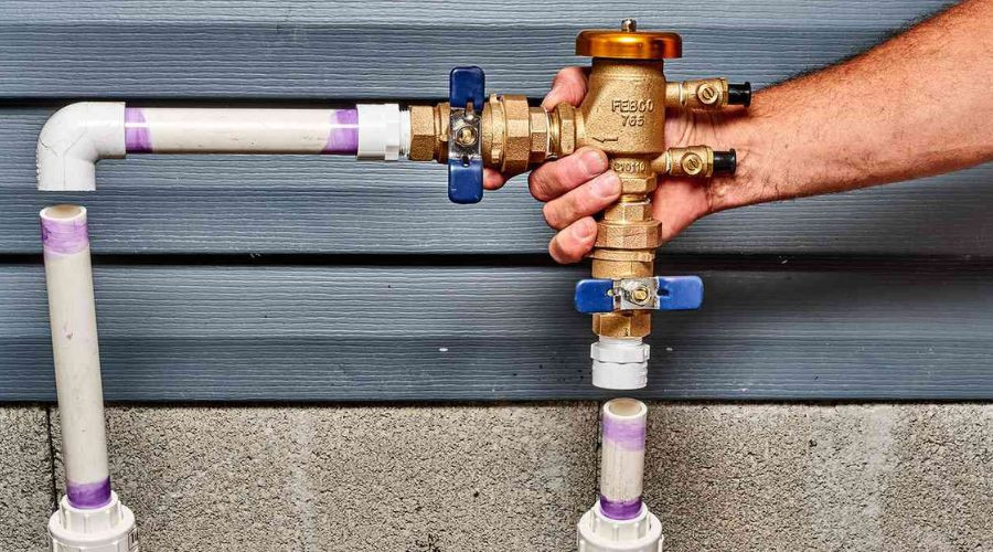 Hand adjusting a brass valve on a plumbing system with PVC pipes, illustrating plumbing maintenance and repair techniques relevant to homeowners.