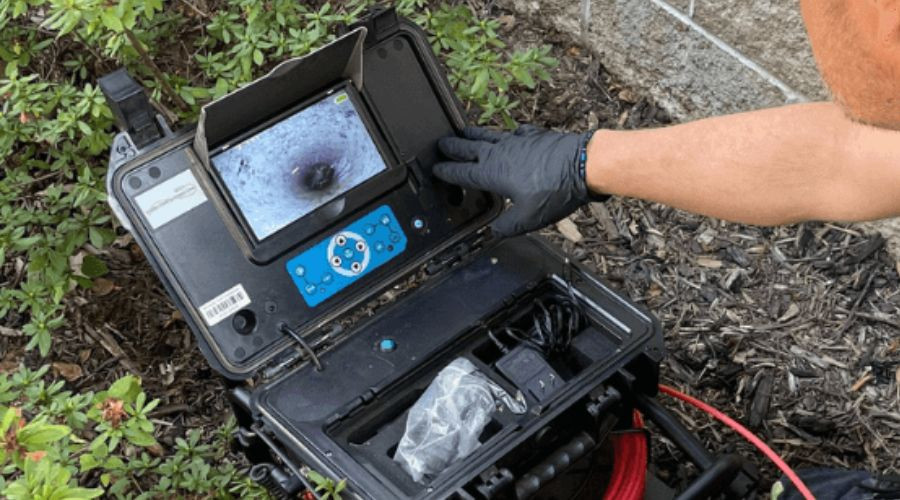 Technician using a sewer inspection camera to detect plumbing issues, with a focus on the screen displaying a close-up view of a pipe.