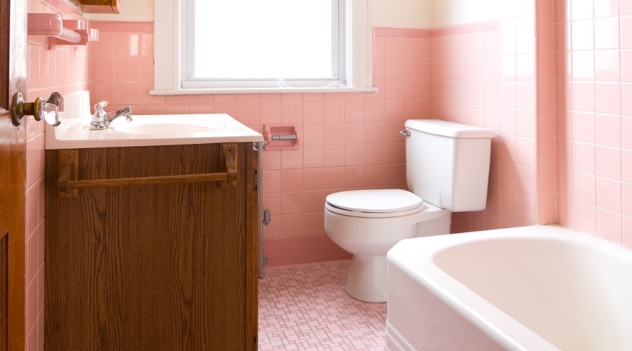Bathroom with pink tiles, toilet, sink, and bathtub, illustrating common plumbing issues in older homes.